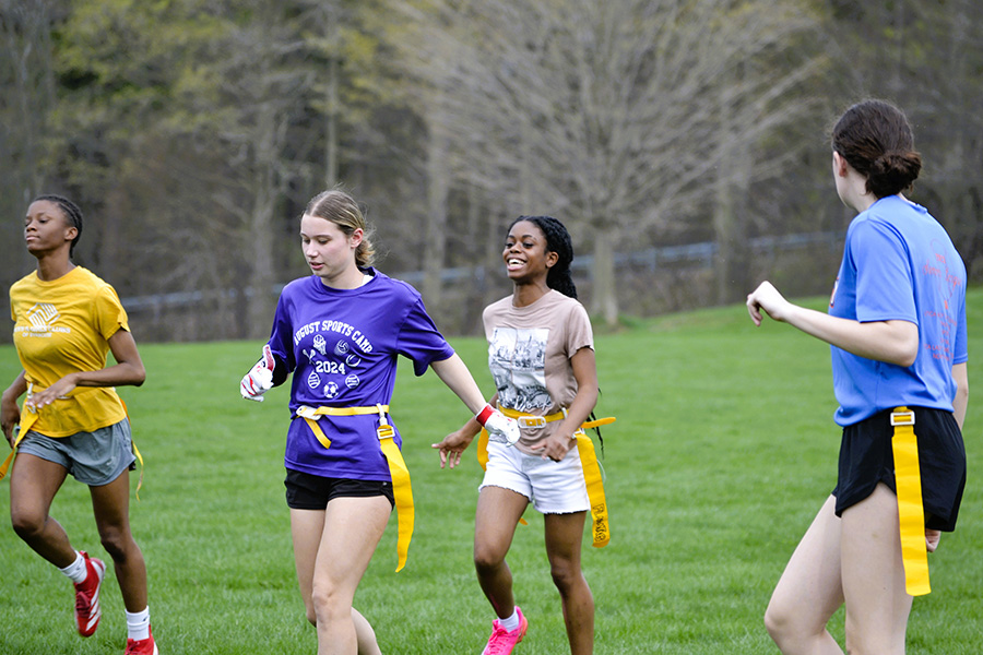 Four students run on field wearing flag football flags.