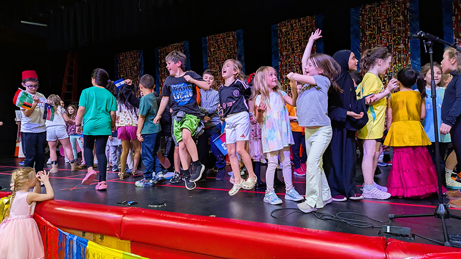 A large group of students dance on stage.