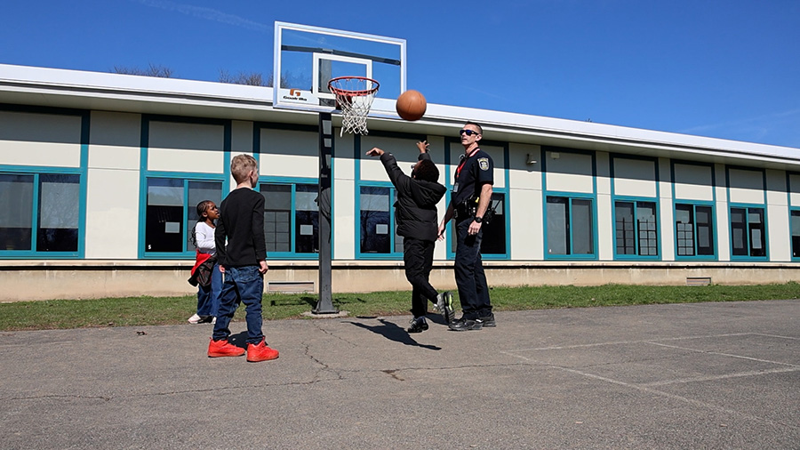 School patrol officer plays basketball with three elementary students.