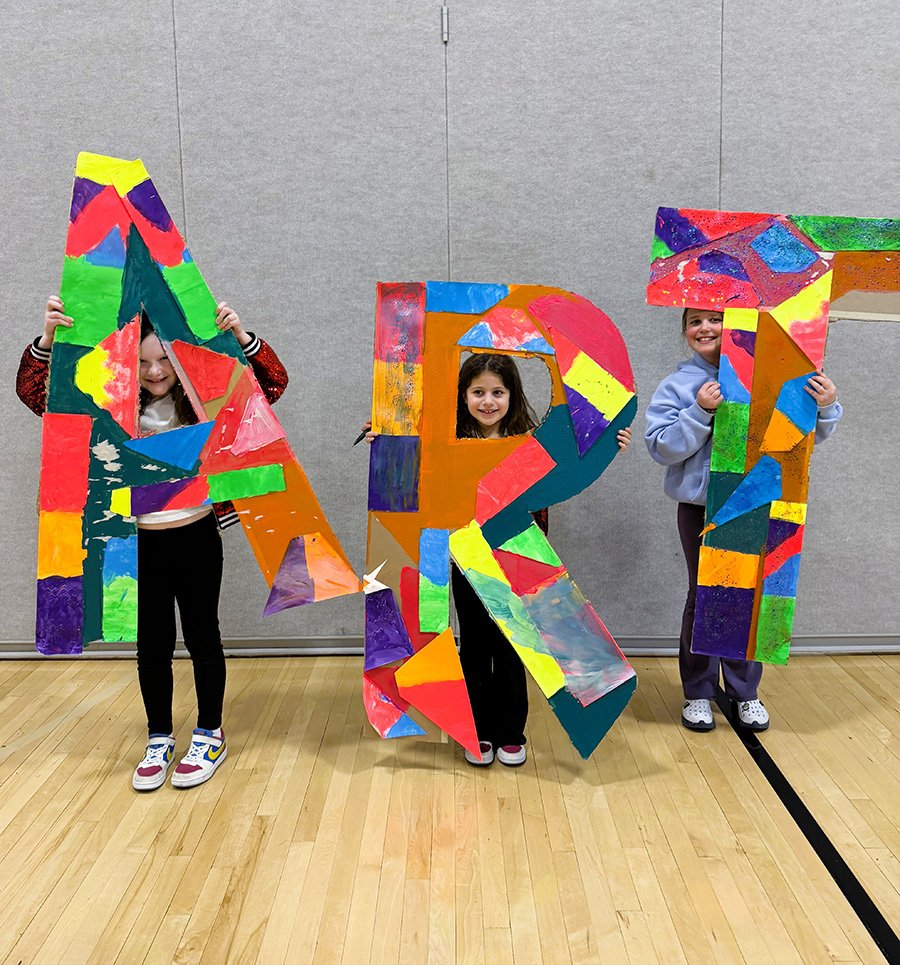 Three students hold large colorful letters that spell art.