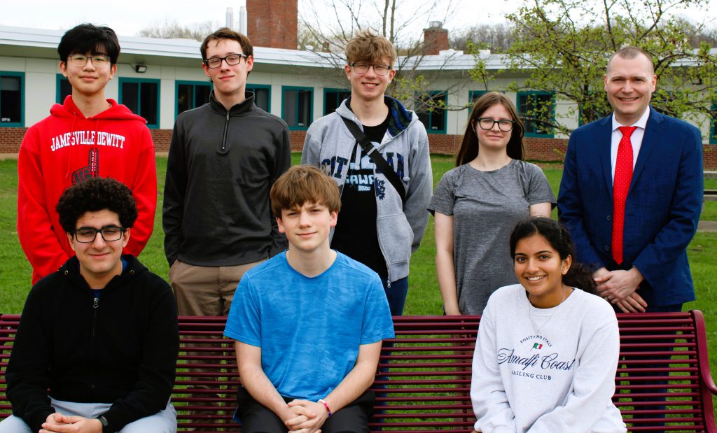 Seven students post for group photo with High School Principal. Some sit on a bench and the others stand behind them.