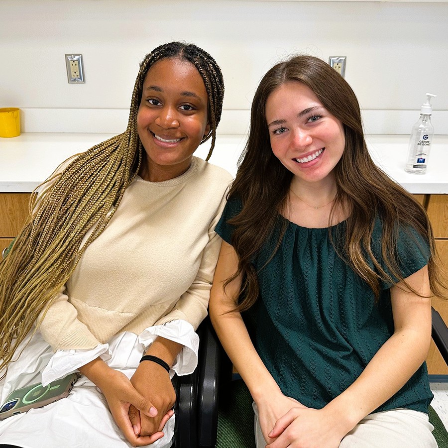 Two students sit and smile