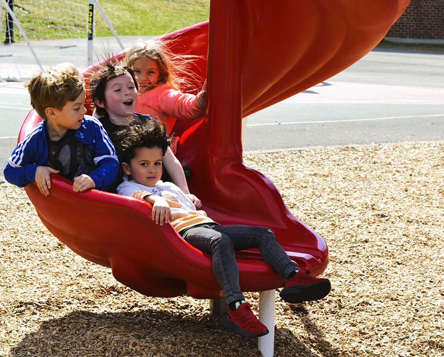 Four students are bunched up and smiling at the end of a slide.