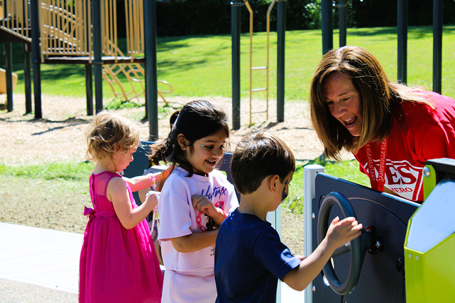 Principal March Baker smiles at three students on playground.