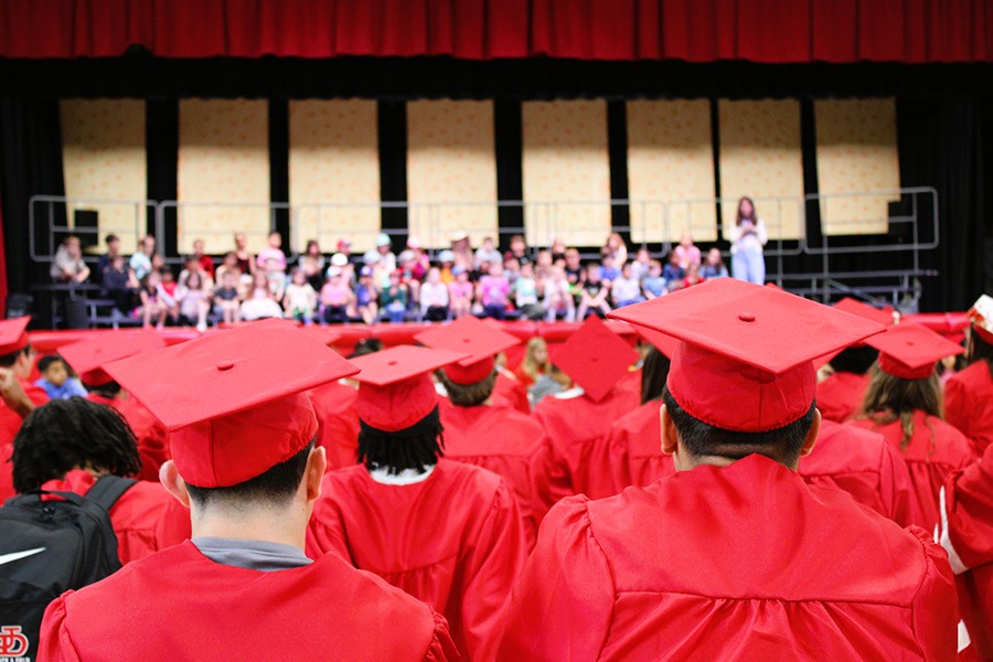 Backs of red graduation caps as students watch elementary performers.