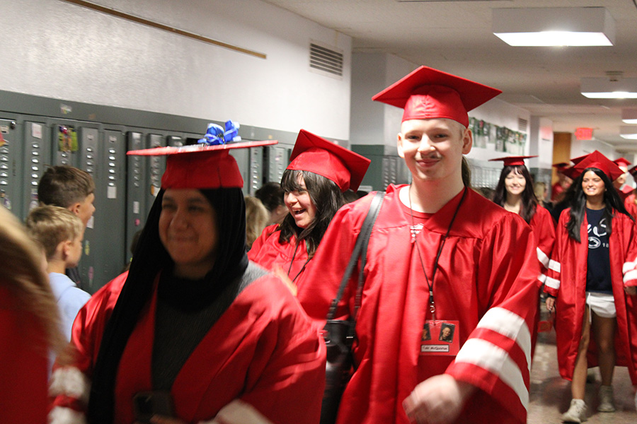 Seniors walk down hallway wearing red cap and gowns.