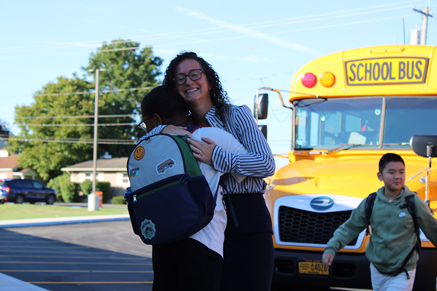 Principal hugs student with bus in background.