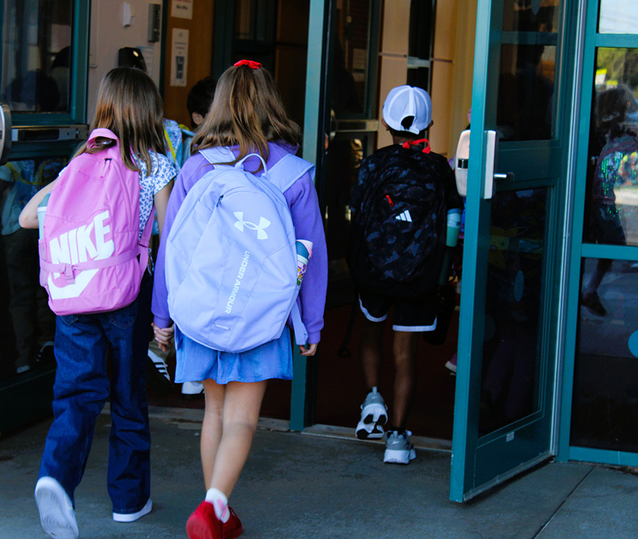 Students walk into school wearing backpacks.