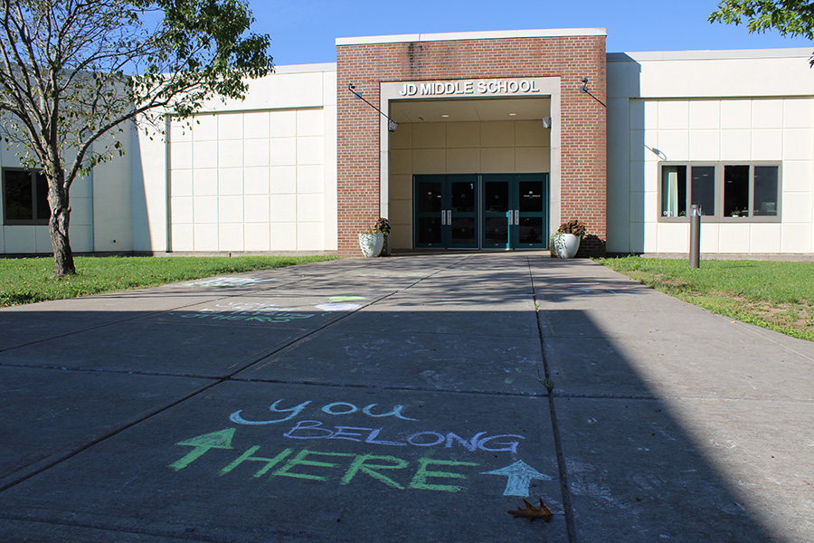 Outside of middle school with chalk on the walkway that says you belong here.