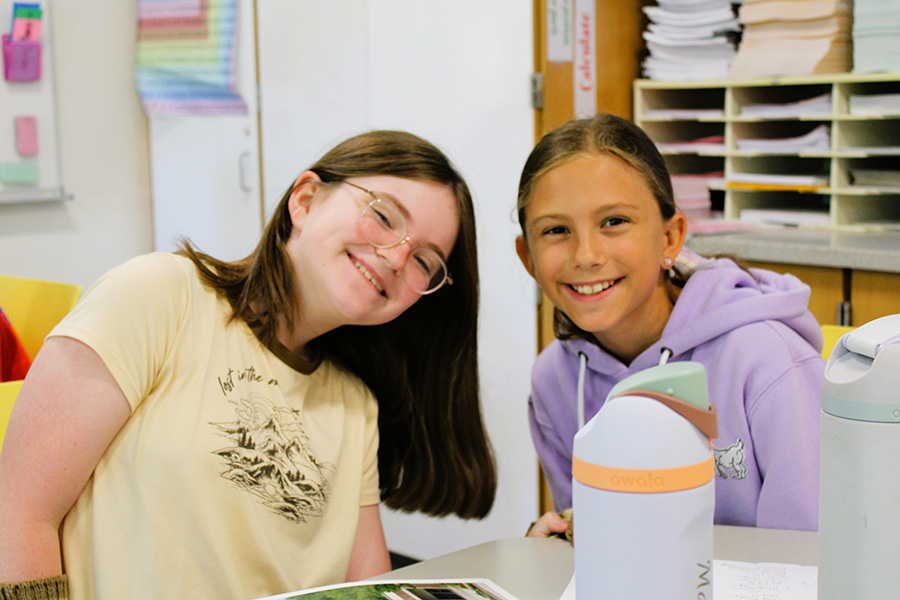 Two students smile at desk.