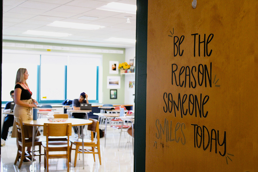 Students and teacher are in classroom, saying on door reads, "Be the reason someone smiles today."