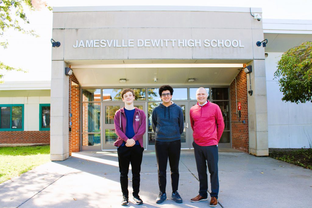 Two students and principal pose for photo outside main entrance of high school.