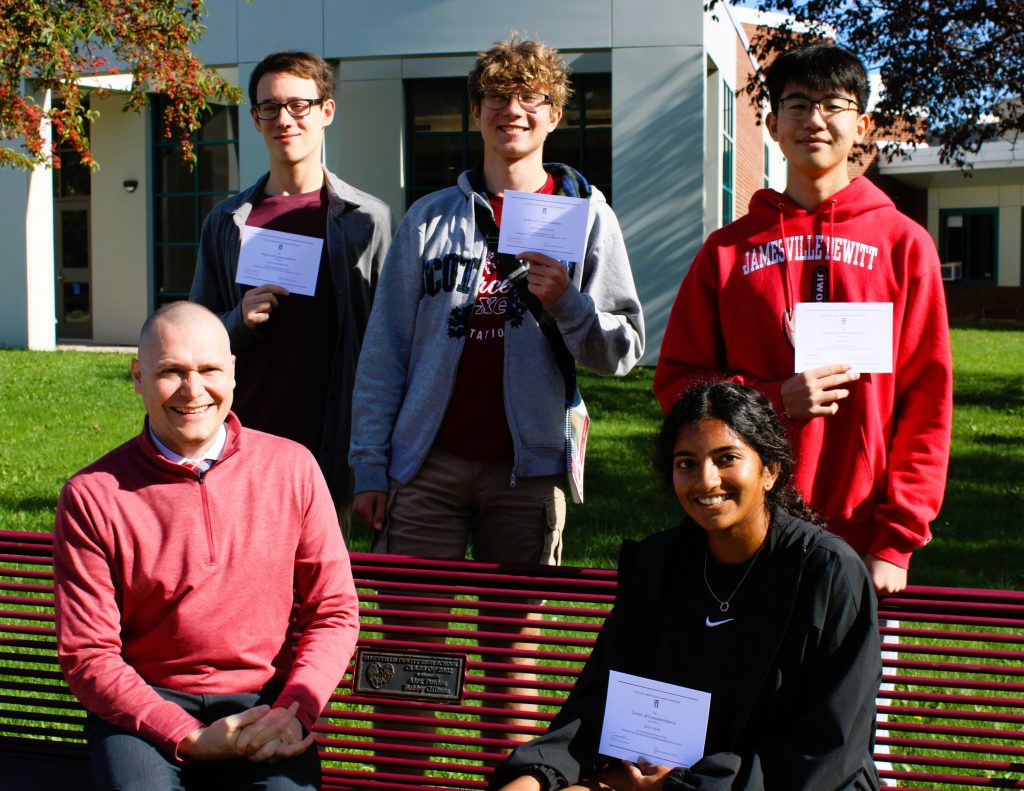 Four students pose with high school principal for group photo in front of school.