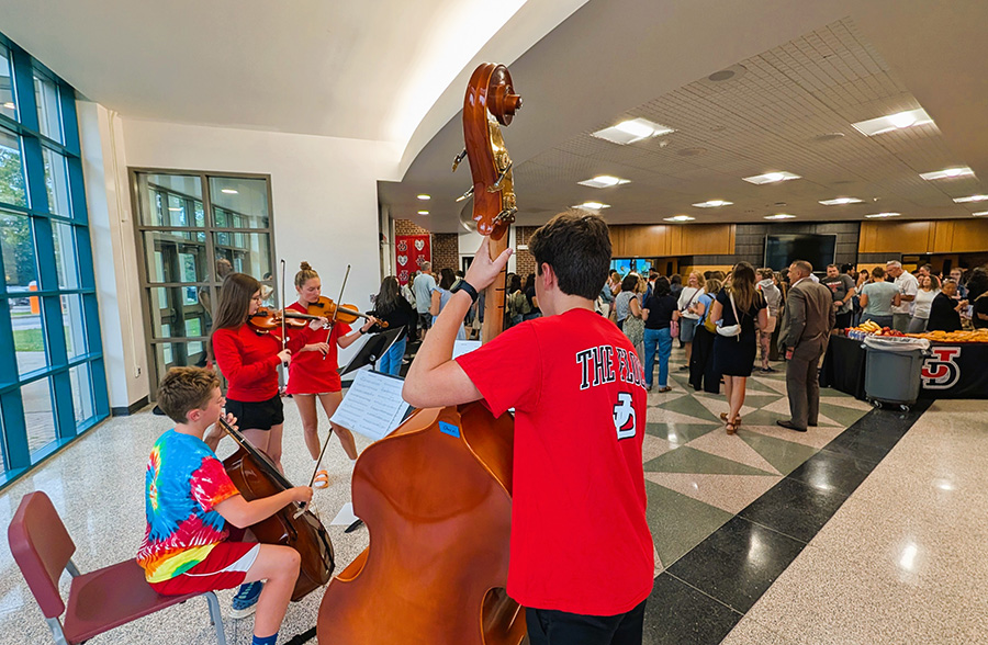Students play instruments as staff walk into auditorium.