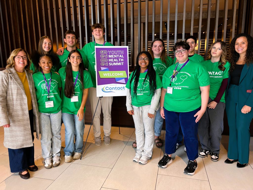 High school students wear matching green shirts and pose with poster and two staff members.